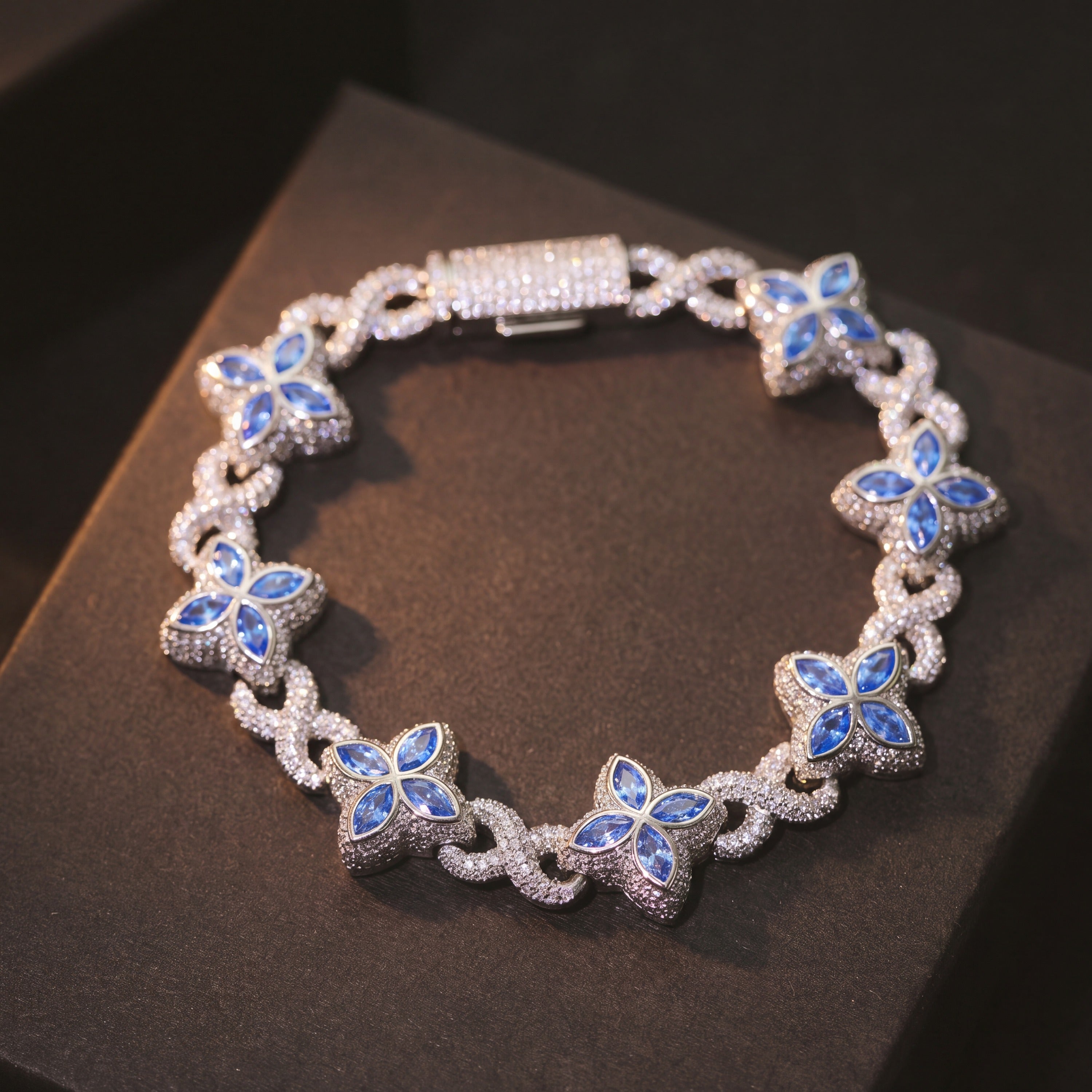 Silver-tone clover flower bracelet on a dark box, showing the full run of blue flowers